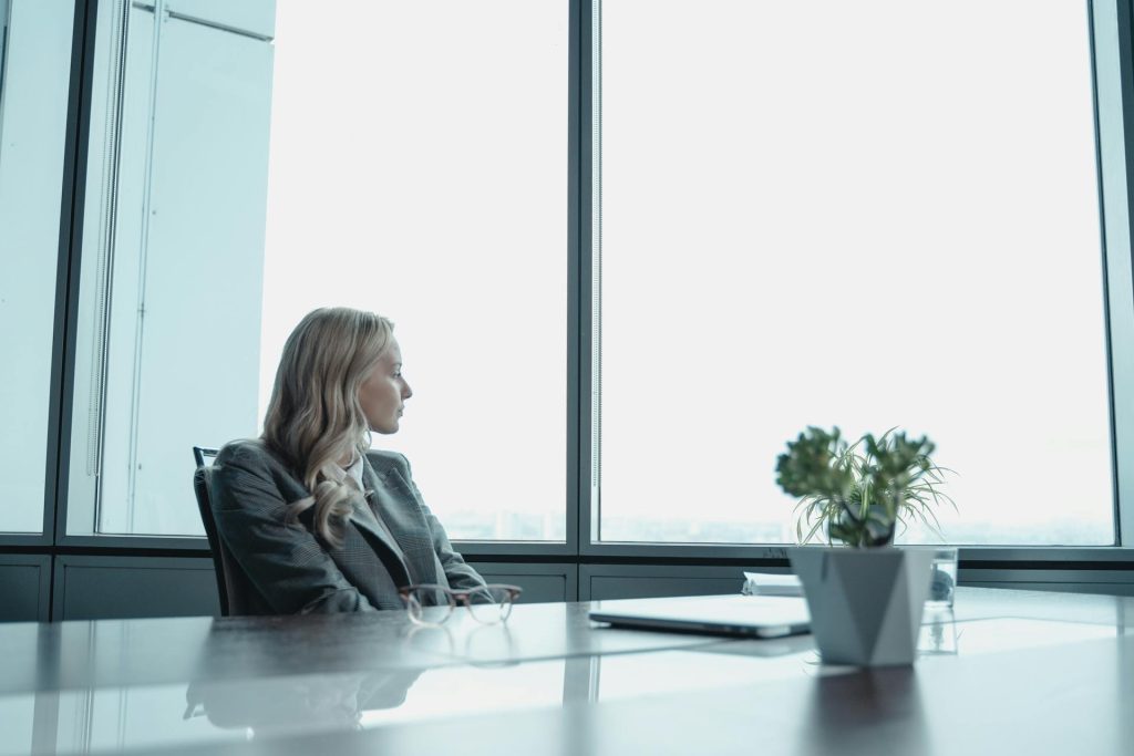 Mujer empoderada sentada en una oficina mirando por la ventana con expresión reflexiva.
