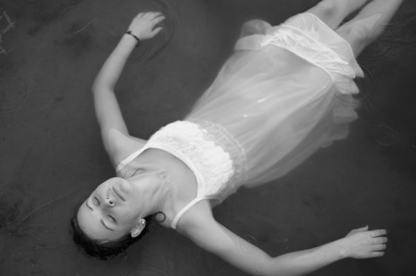 Mujer flotando sobre el agua con los ojos cerrados, simbolizando la validación emocional y la calma interior para dejar de sentirse demasiado
