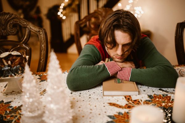 Hombre sentado en una mesa navideña con expresión de tristeza y desconexión, representando la ansiedad navideña y la presión emocional de diciembre.