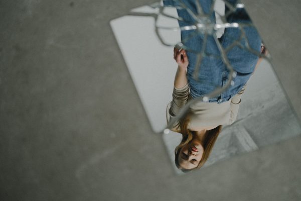 Reflejo invertido de una mujer observándose a sí misma en un espejo roto, representando la exploración del pasado, la identidad y los patrones emocionales aprendidos en la infancia.