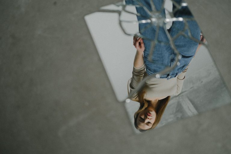 Reflejo invertido de una mujer observándose a sí misma en un espejo roto, representando la exploración del pasado, la identidad y los patrones emocionales aprendidos en la infancia.
